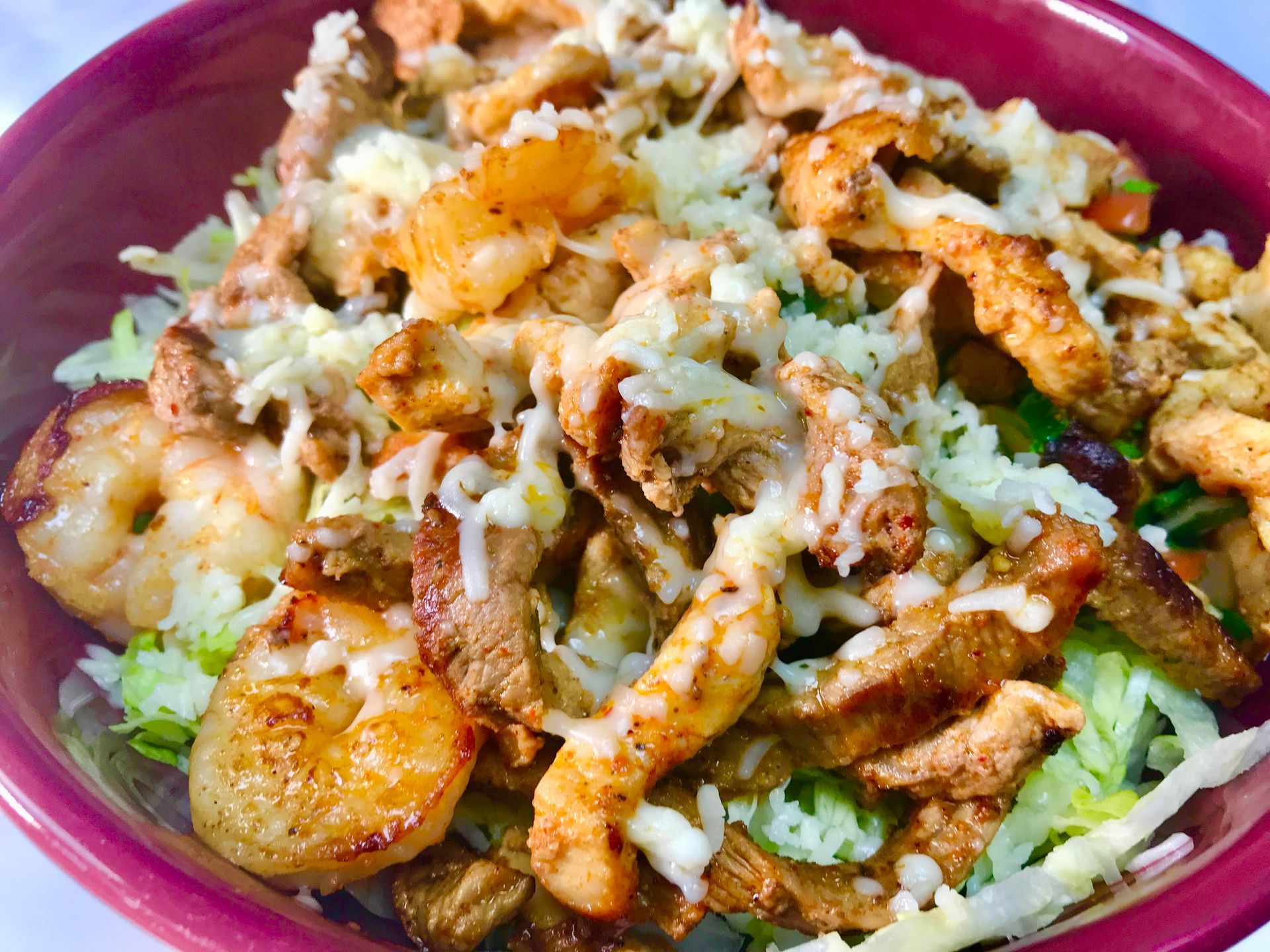 Bowl of food with shrimp, chicken, and shredded cheese on top of lettuce.