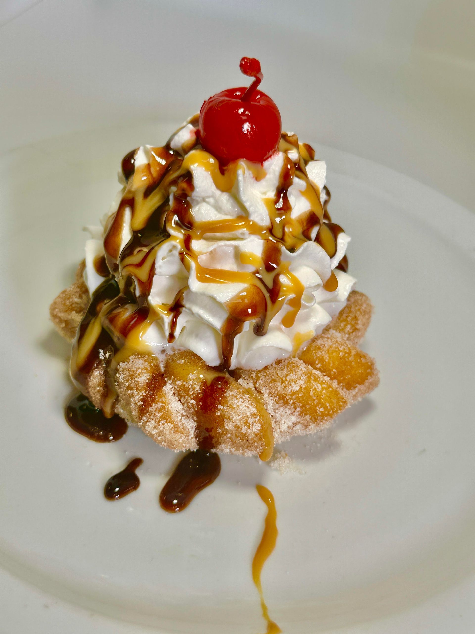Pastry topped with whipped cream, caramel, chocolate sauce, and a cherry.