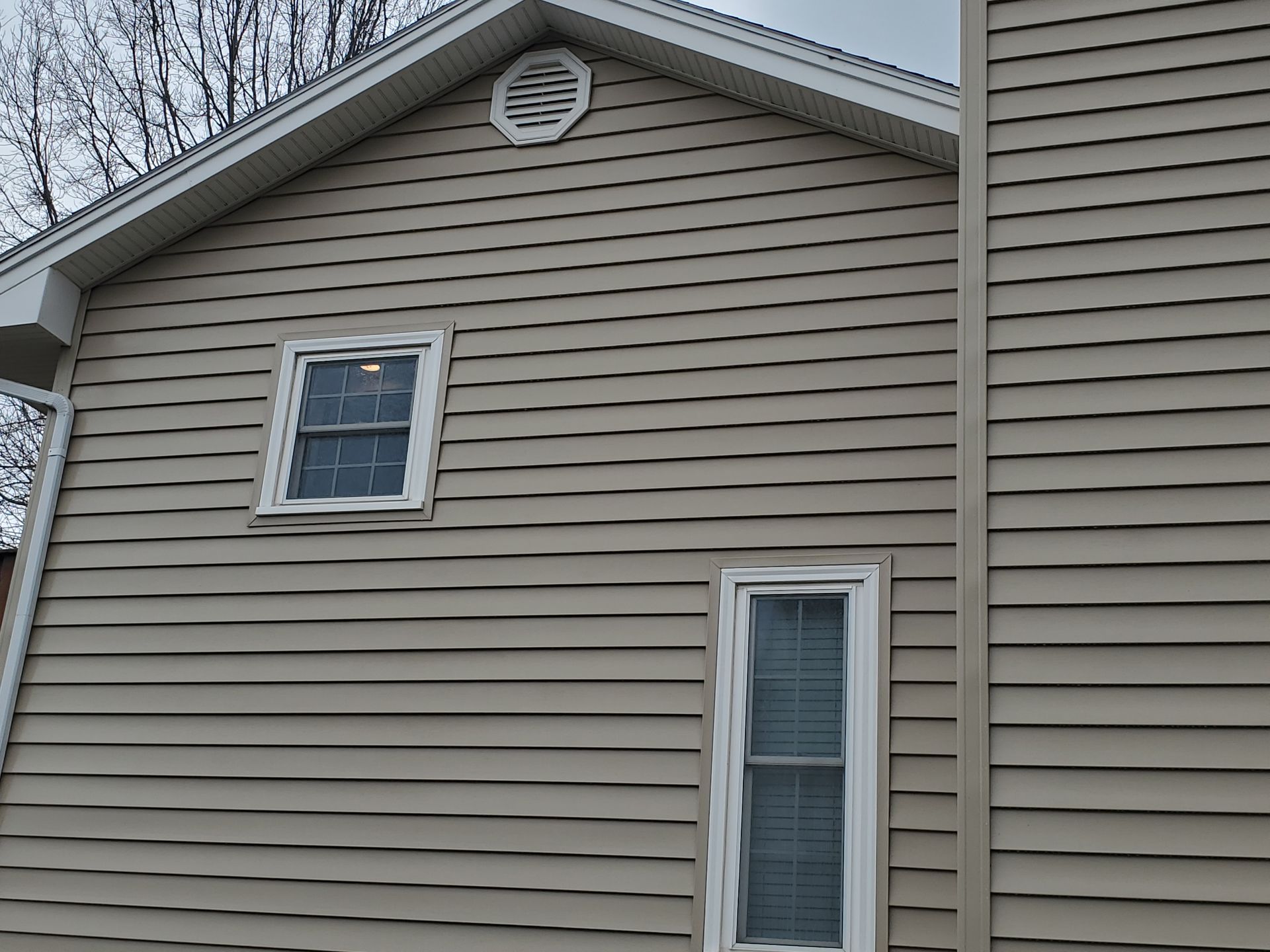 Tan house siding with two windows and a small attic vent under the roofline