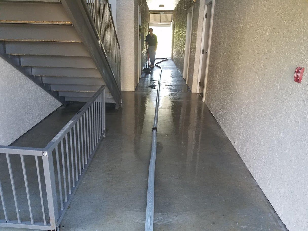 Narrow apartment hallway with wet floor, stairs on the left, and a person in the distance near a bright doorway