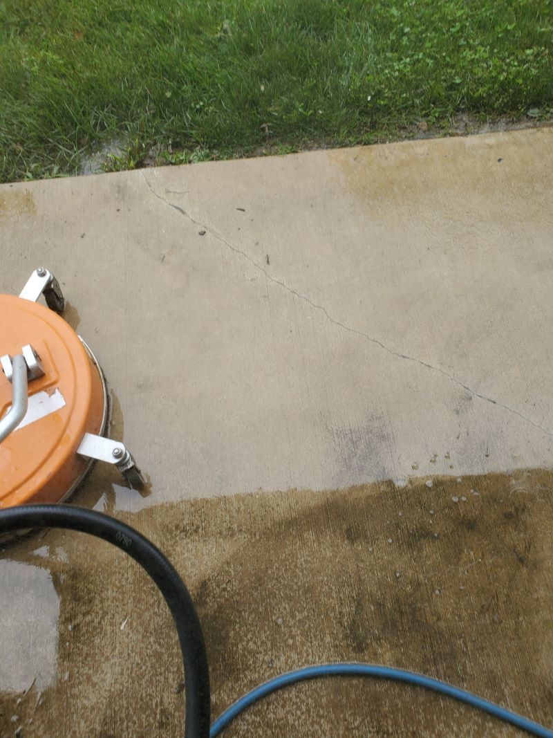 Concrete patio beside grass with a partially visible orange-and-white lawn machine and black hose.