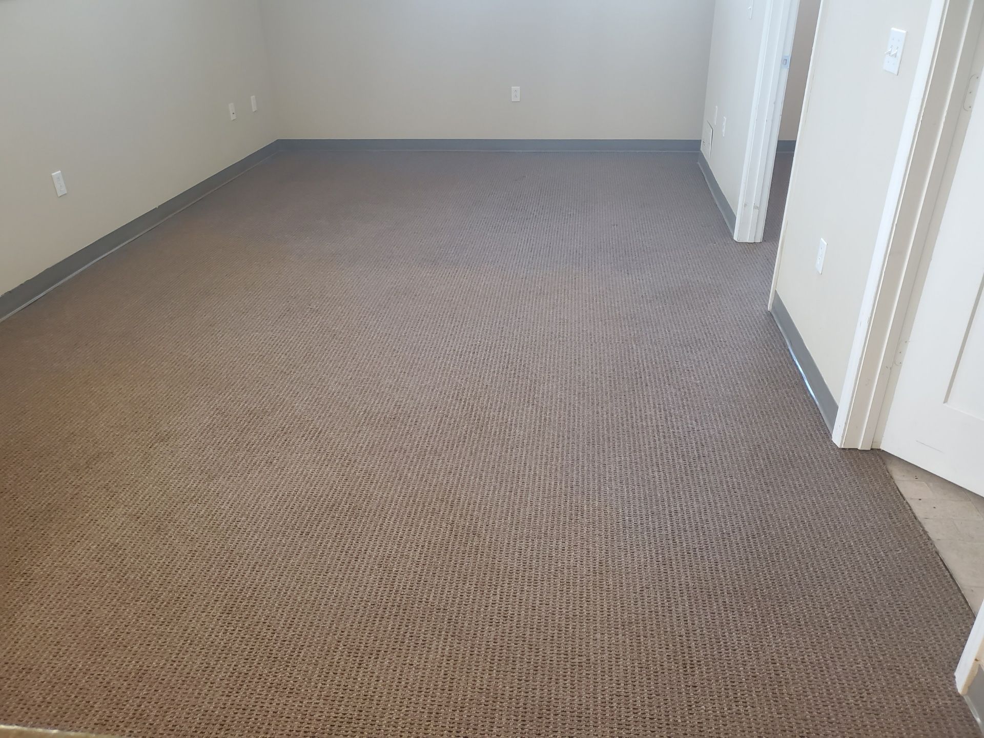 Empty beige-carpeted hallway with white walls and doors leading to a room