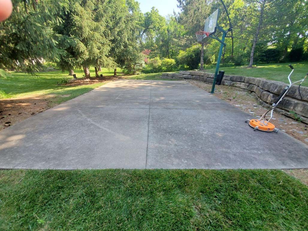 Wide concrete path in a green park beside a stone wall and lawn, with an orange object on the right.