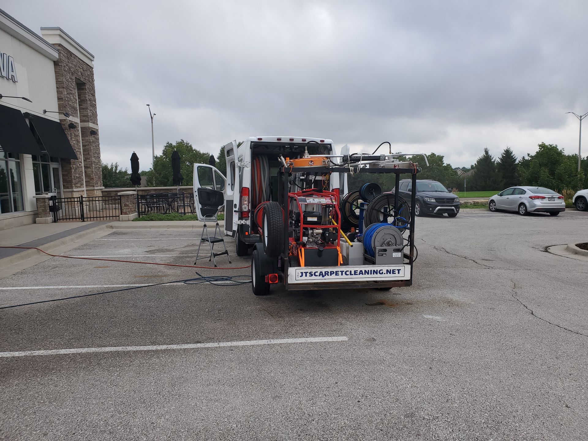 Power washing utility truck with mounted equipment parked in a lot beside a building under cloudy skies.