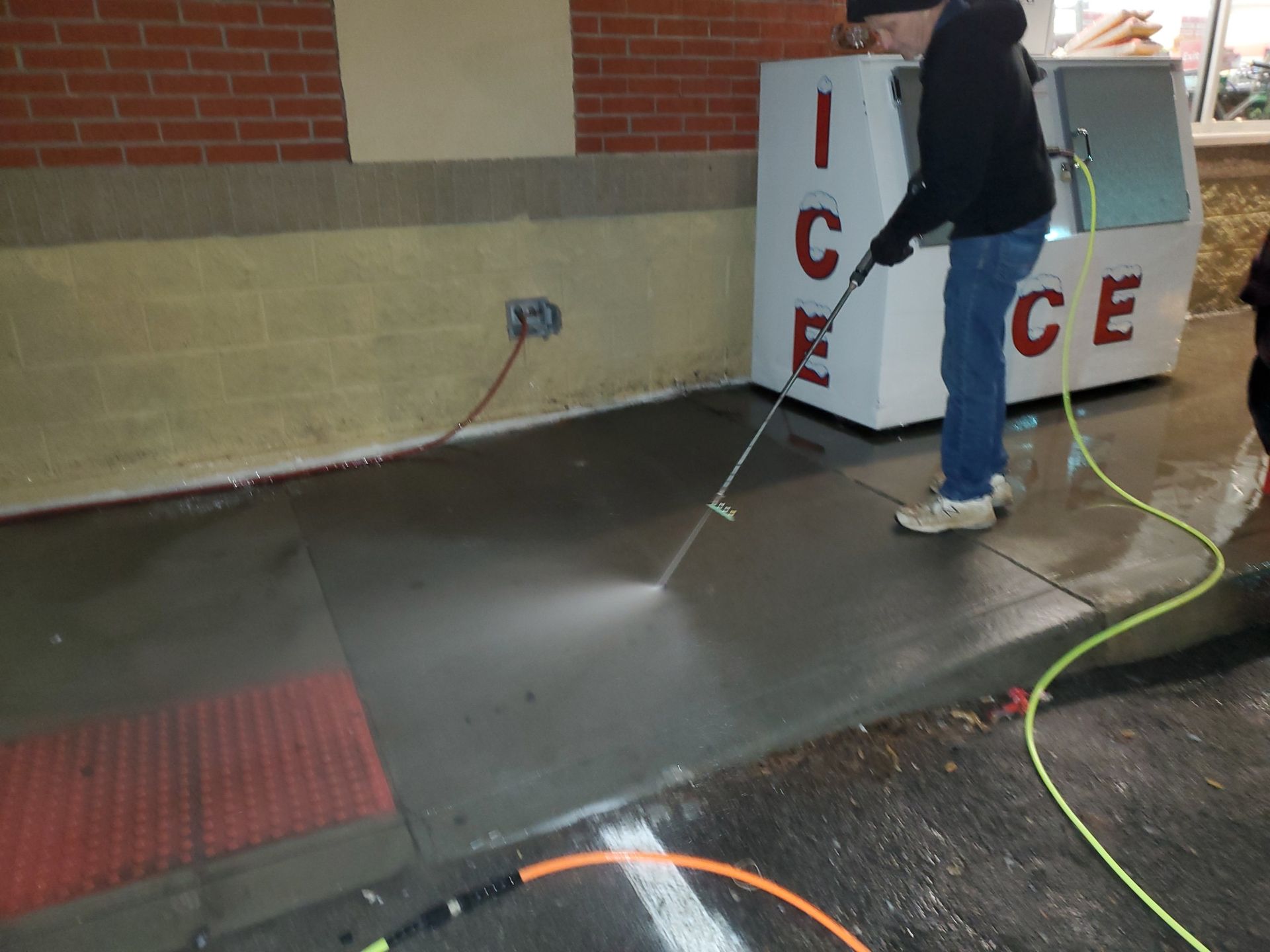 Person washing a concrete floor beside an ICE machine with a hose.