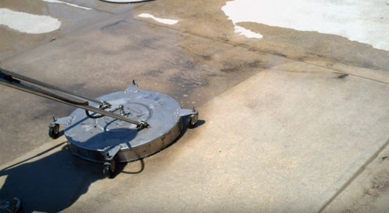 Blue vehicle winch on pavement beside a light-colored concrete wall and wet ground