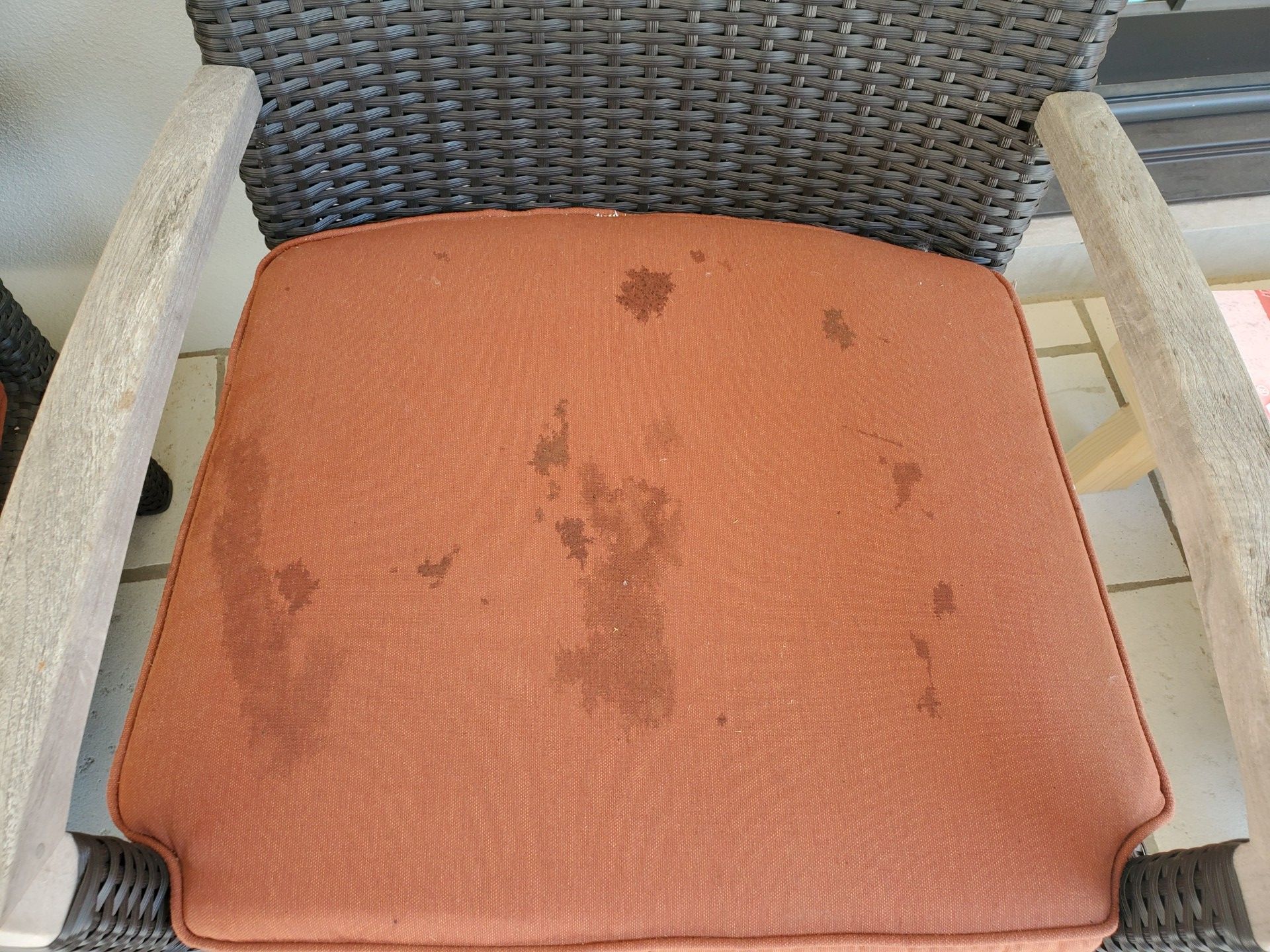 Orange chair cushion with dark stains and a wicker backrest and light armrests