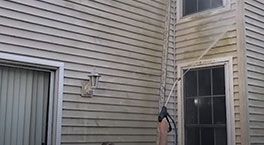 Man climbing a ladder beside a tan house near a window and siding.