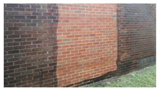 Brick wall with a lighter rectangular patch in the center and grass along the bottom edge