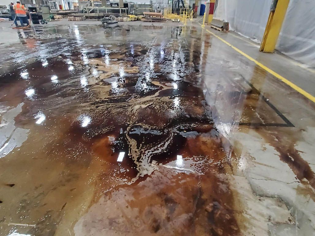Wet industrial floor with a large rust-colored spill and reflections in a warehouse aisle