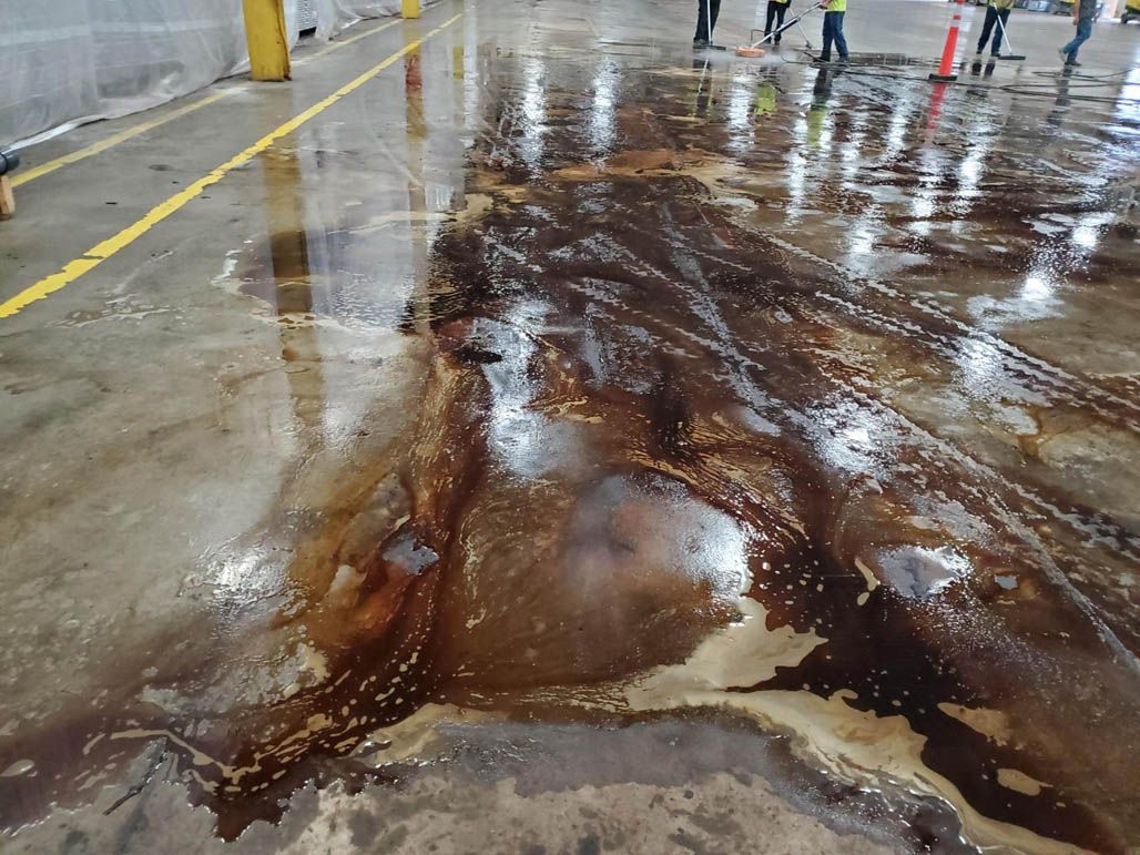 Midway through power washing the concrete floor in a warehouse or garage, with a few people in the background