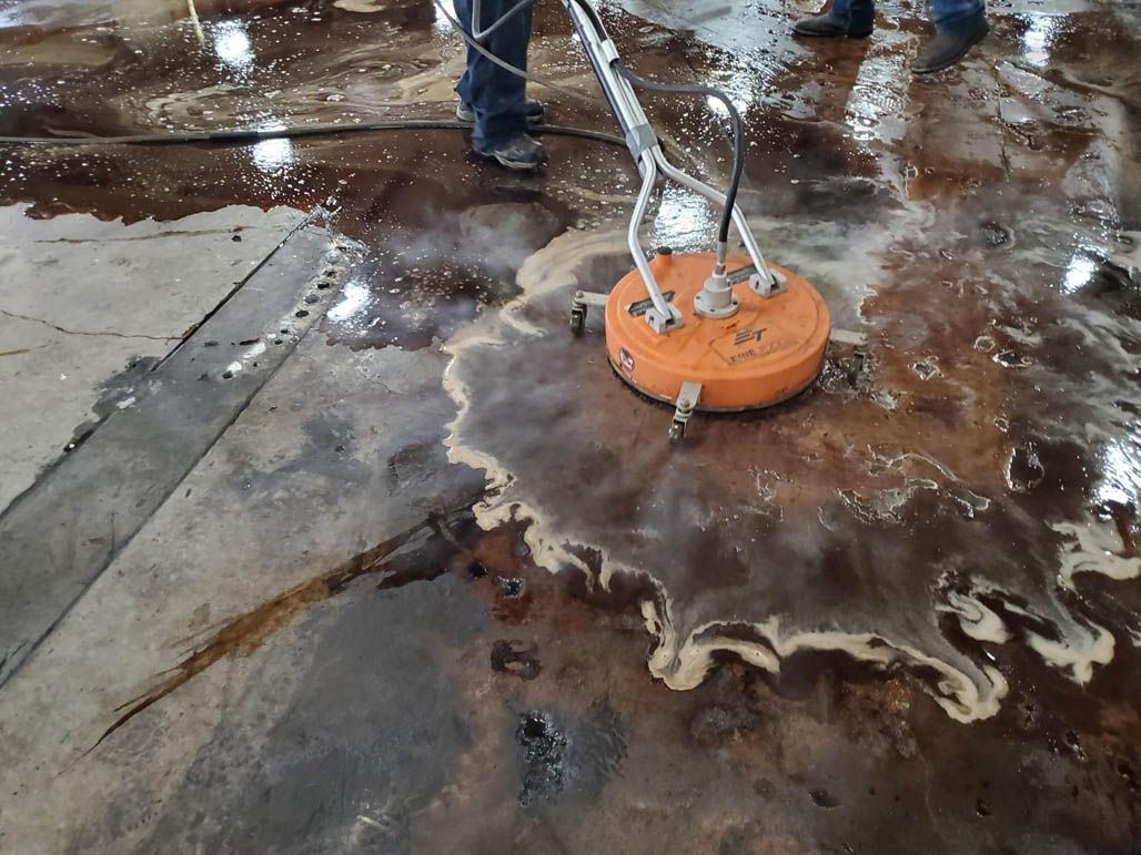 Orange pressure washer cleaning a wet concrete floor with foamy water splash