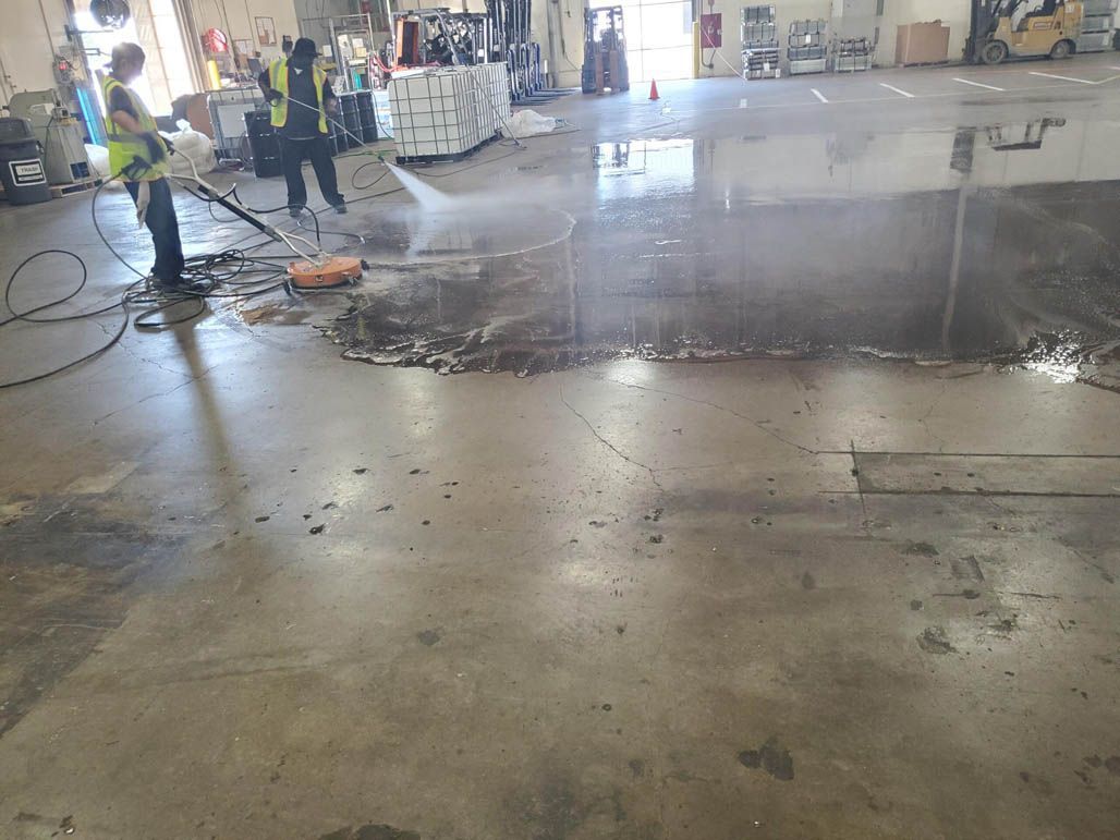 Workers power washing concrete floor in a warehouse or factory after a spill