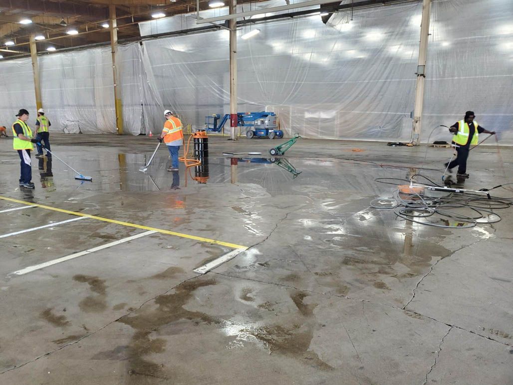 Workers in safety vests inspect a wet warehouse floor after heavy amounts of oil have been removed.