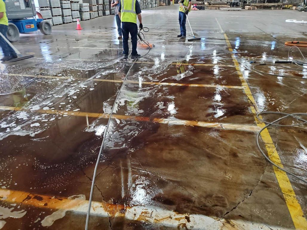 Workers washing a warehouse floor with hoses in a parking/loading area