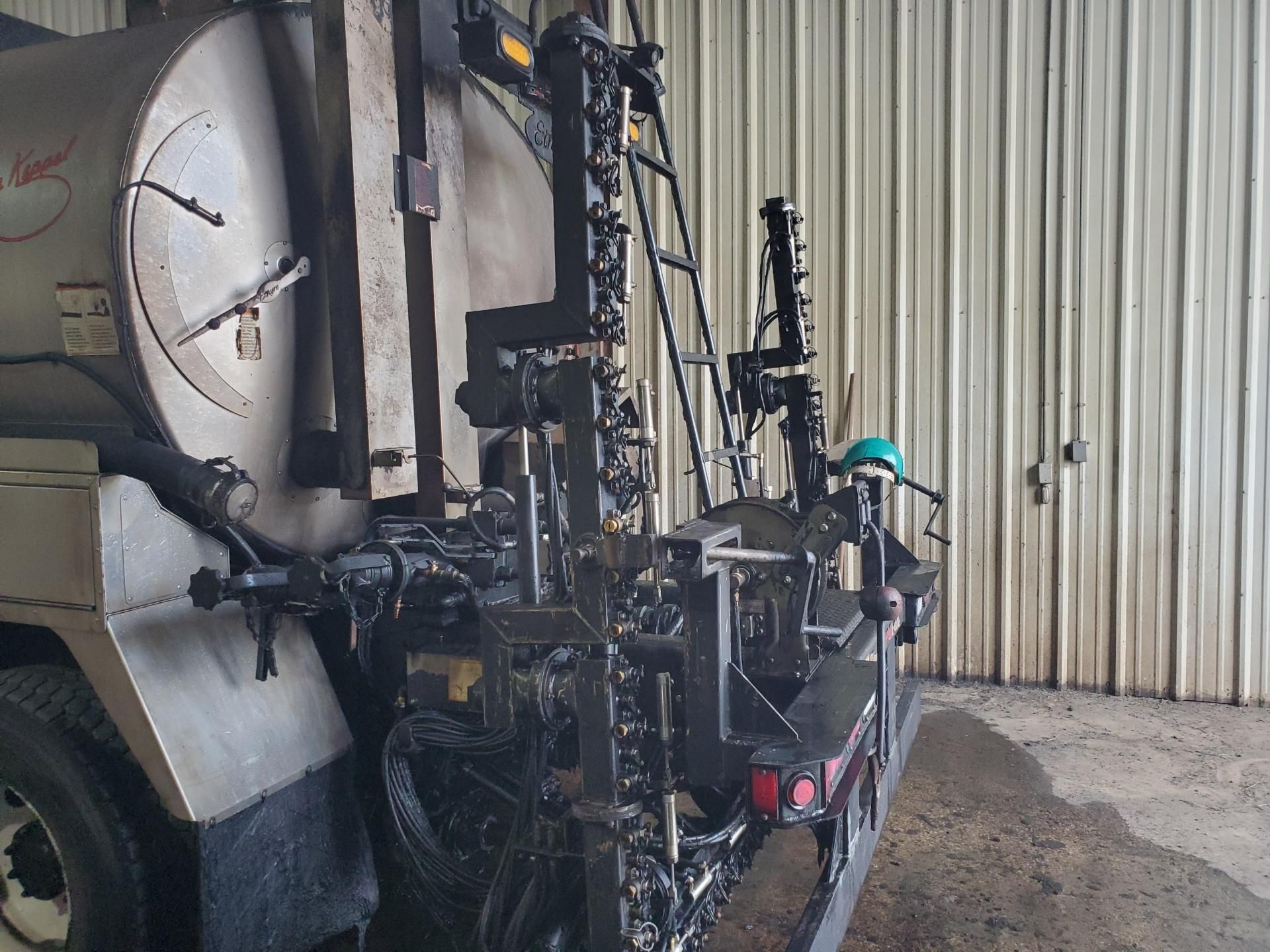 Industrial machine or farm equipment with black framework beside a large white tank in a metal shed