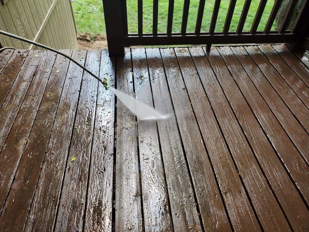 Wooden deck being sprayed with water, with wet boards and a grassy yard in the background