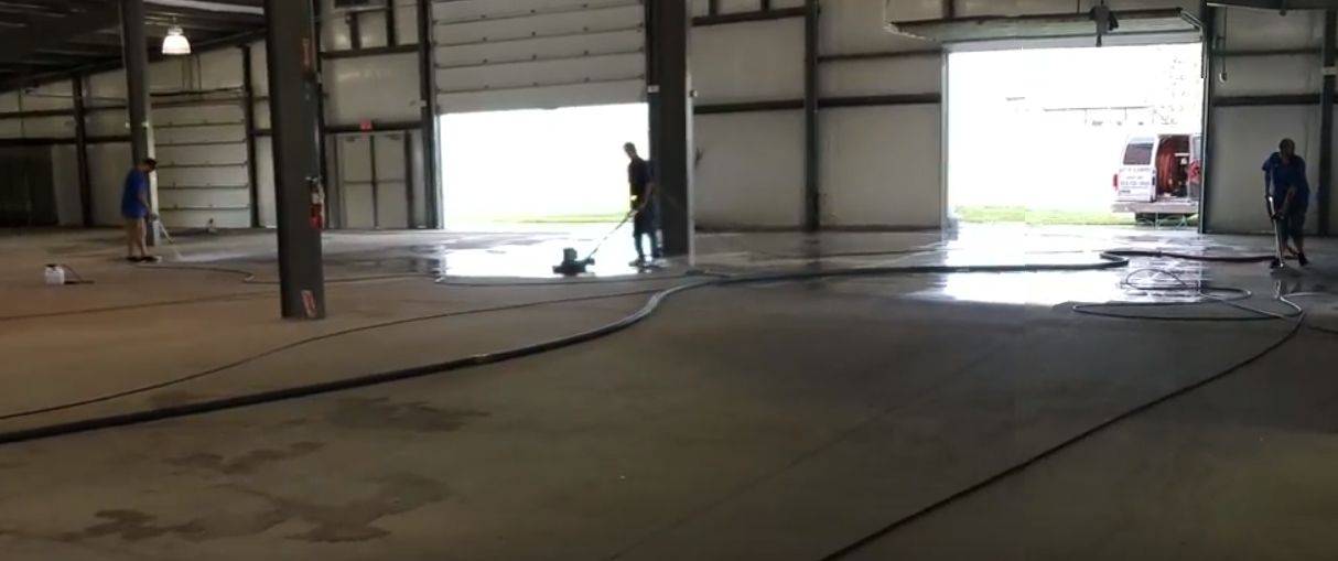 Large warehouse interior with open doors, wet floor, and a few people in the distance.