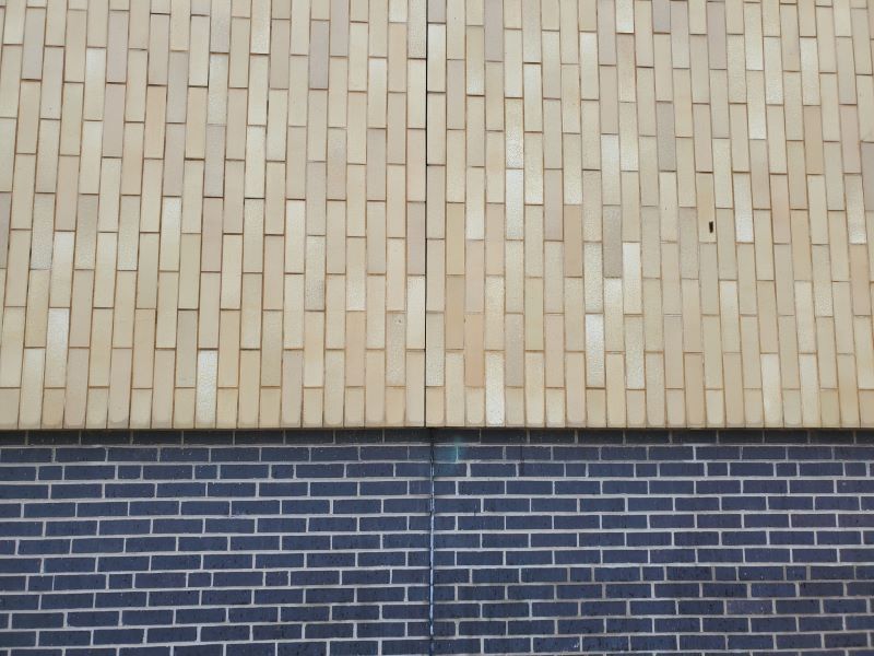 After teal graffiti tags were removed from a tan brick wall above a dark blue brick base