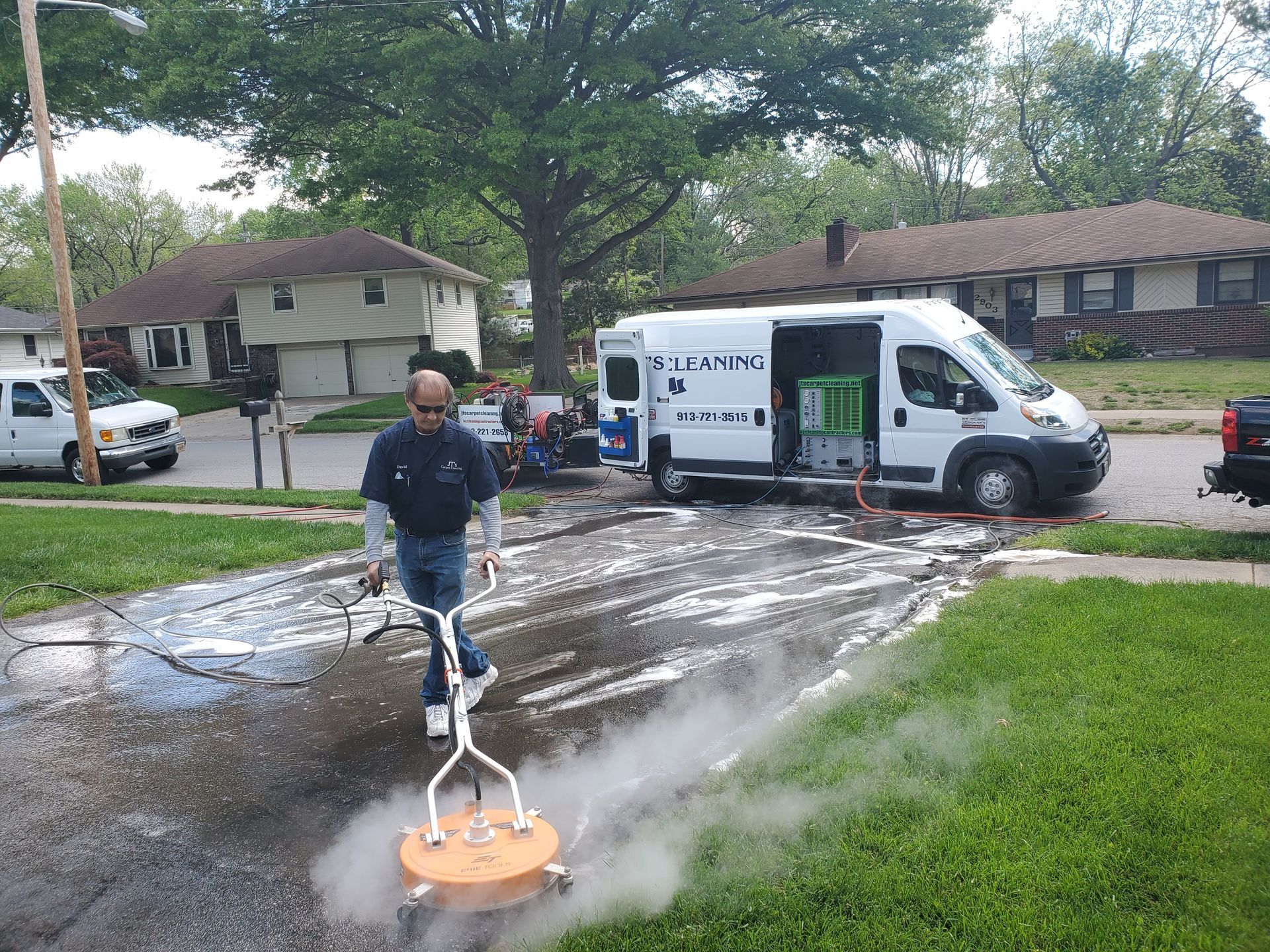 Worker pressure washing a driveway beside a white service van in a suburban neighborhood
