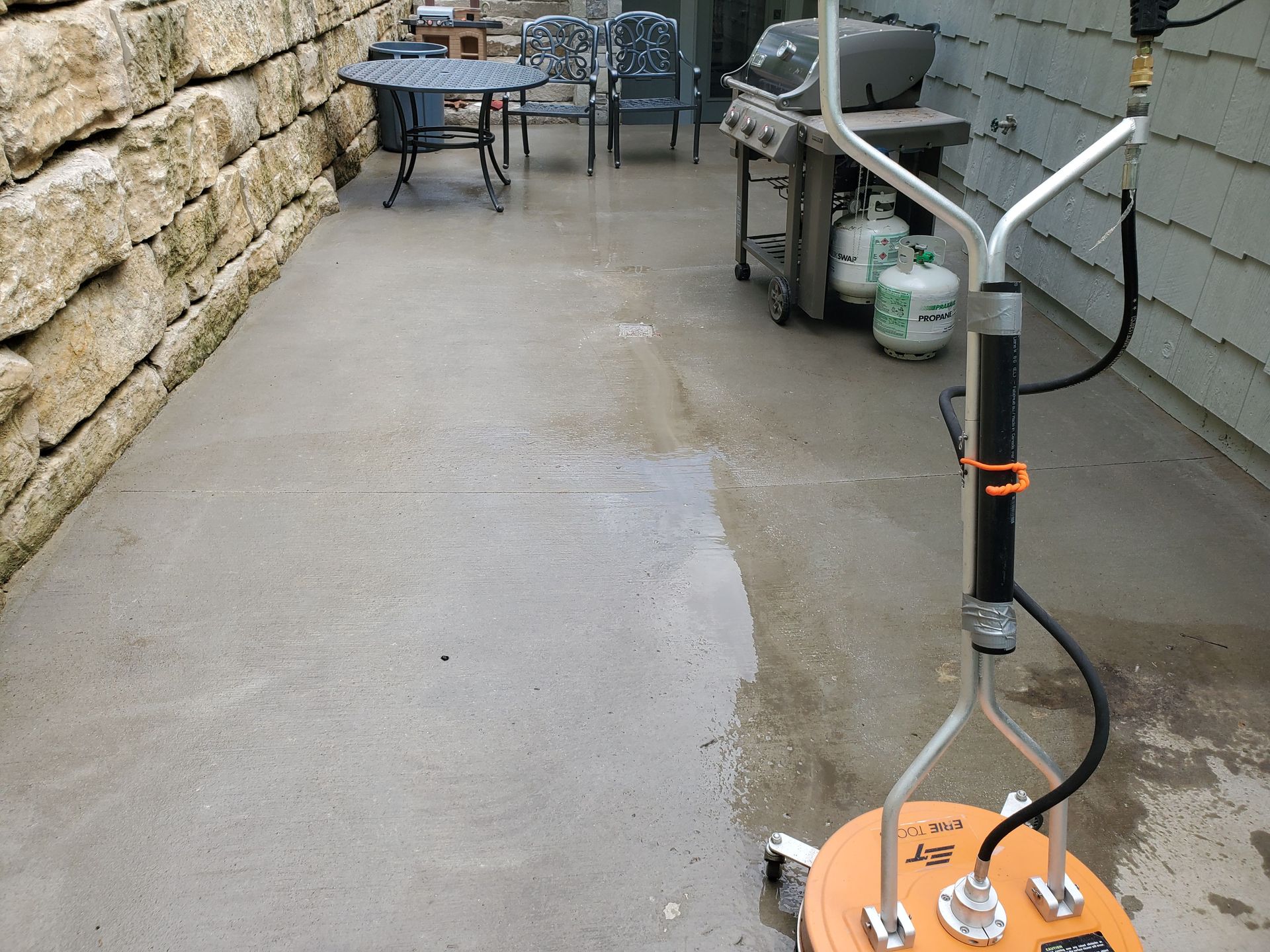 Power washed outdoor walkway with a metal stand and orange base beside stone and siding walls