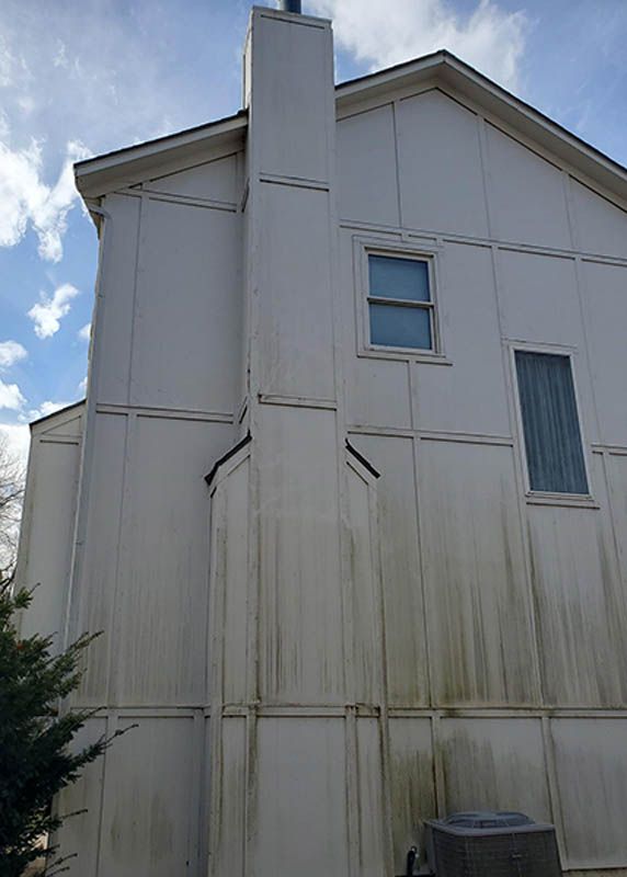 Side view of a weathered white house with a chimney and stained siding under a cloudy sky