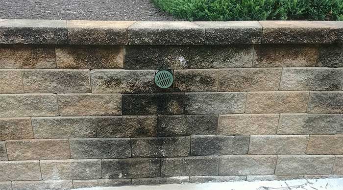 Stone retaining wall with a green drain vent and dark water stain below it