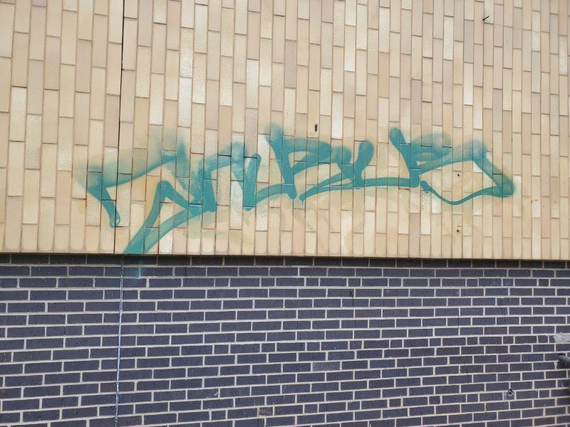 Teal graffiti tags on tan brick wall above a dark blue brick base