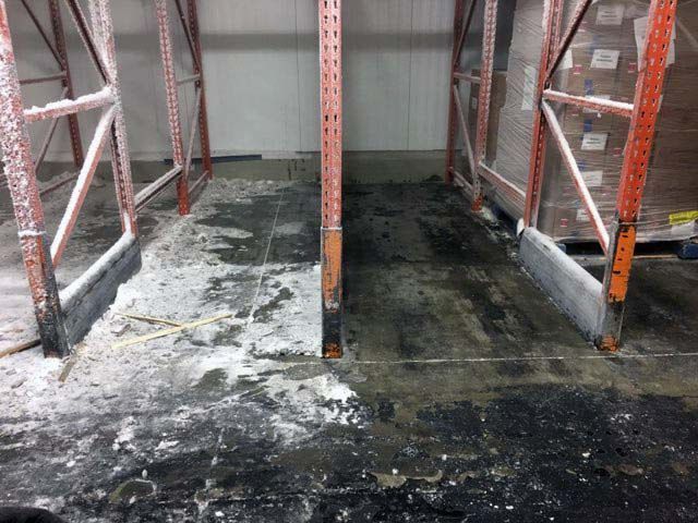 Water-damaged warehouse floor between metal shelving racks with dark stains and mold-like residue