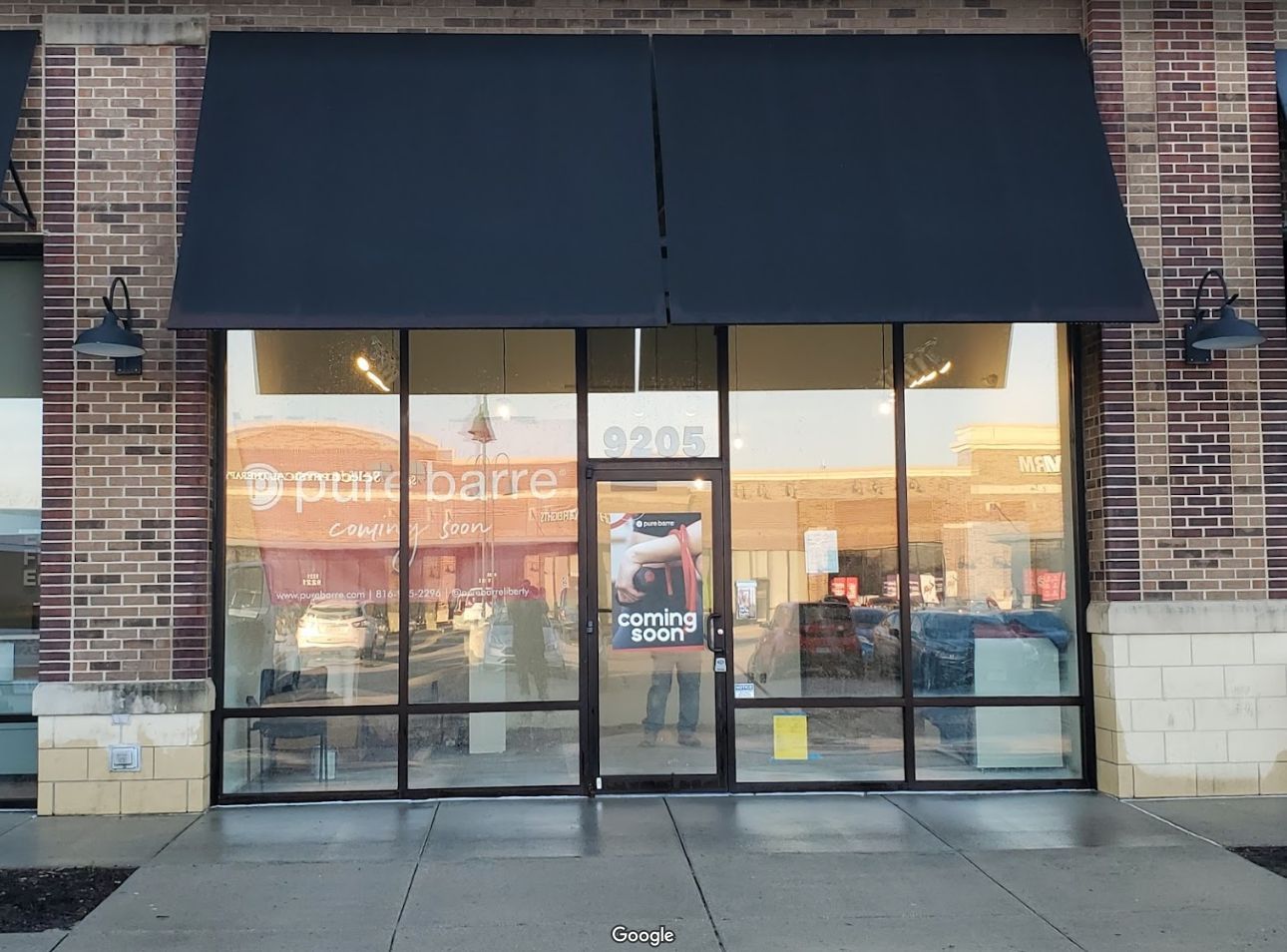 Storefront with black awning and glass doors on a brick building, lit from inside at dusk