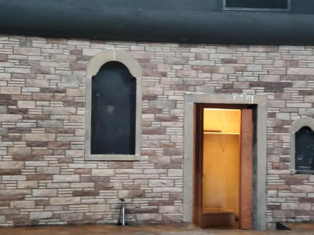 Stone building exterior with arched windows and a warmly lit open doorway at dusk