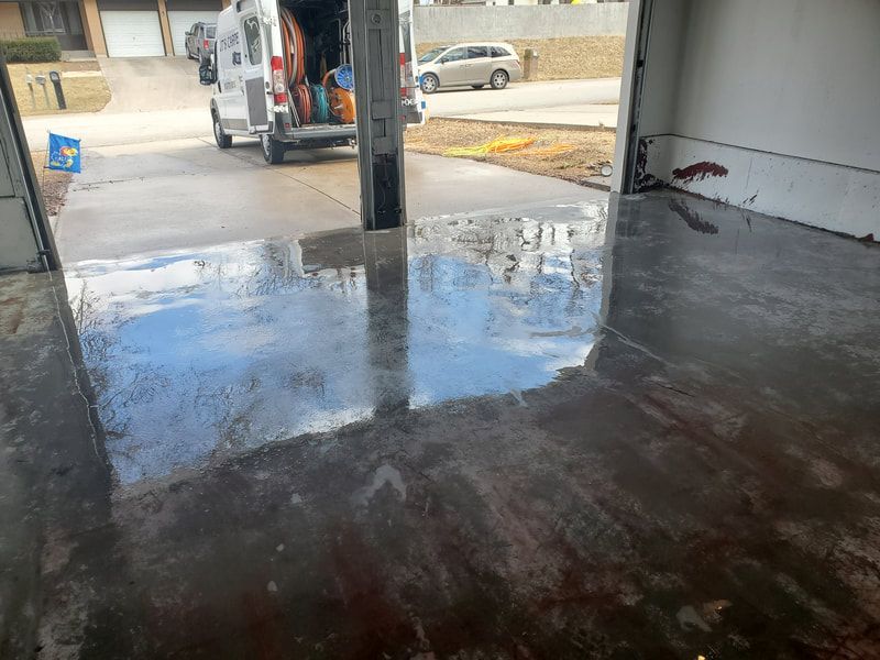 Shiny wet concrete floor inside a garage, with a support column and a vehicle visible outside.