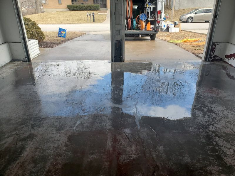 Wet garage floor reflecting an open garage and a truck outside, with a driveway and street beyond.