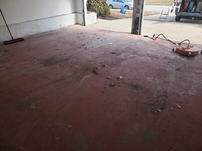 Empty garage with a worn red concrete floor and an open doorway to the outside.