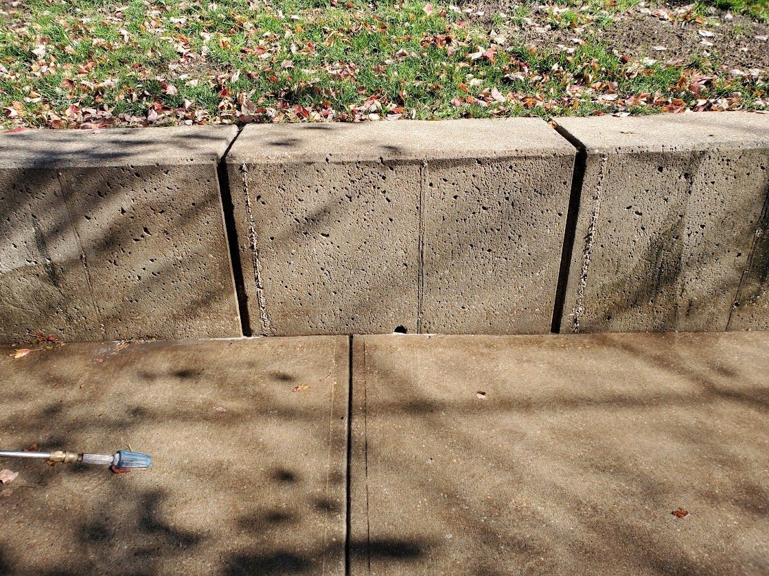 Concrete curb beside a sidewalk with grass and fallen leaves behind it, and a long crack in the pavement