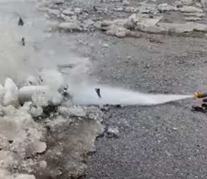 Fire hose spraying water onto melting snow and ice on a wet road
