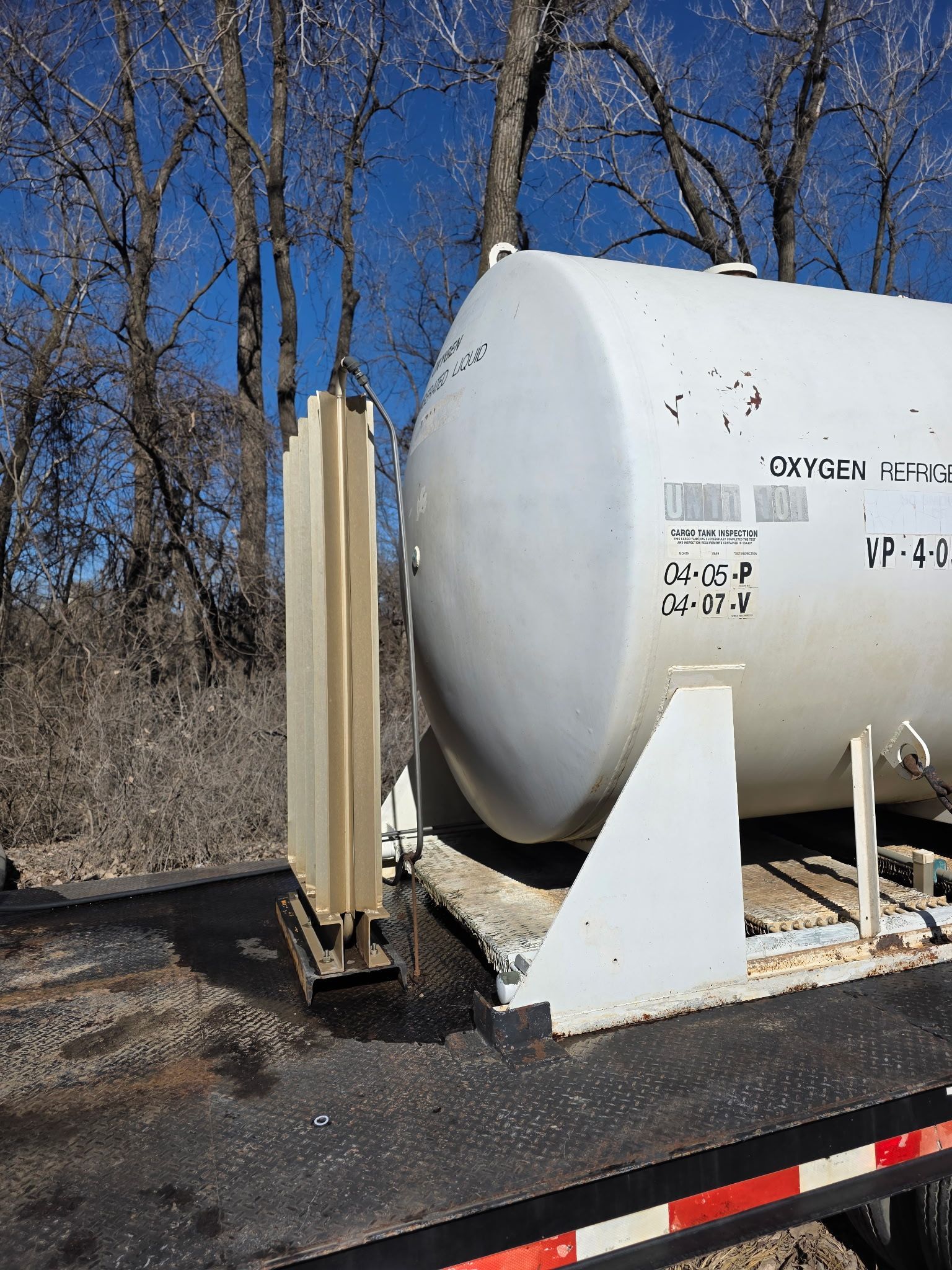 After power wash cleaning a white cylindrical tank on a flatbed trailer beside a beige cabinet, outdoors on a sunny day.