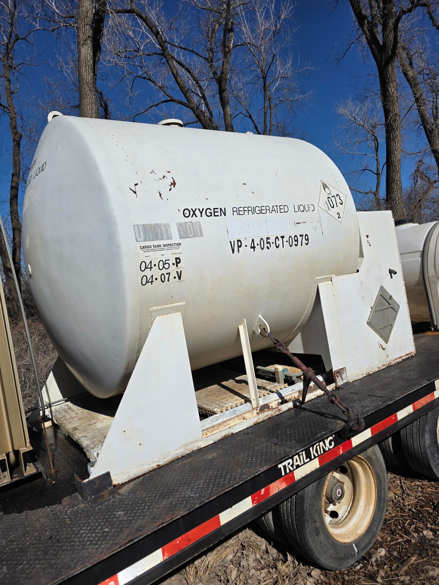 After power wash cleaning a large white cylindrical tank strapped to a trailer outdoors in a wooded area.
