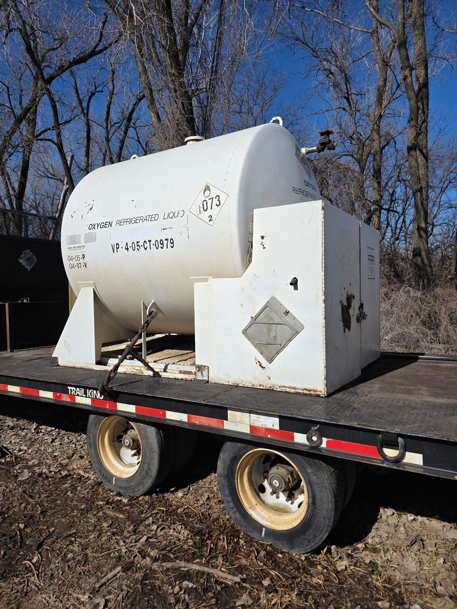 After power wash cleaning a white cylindrical tank mounted on a flatbed trailer outdoors among bare trees