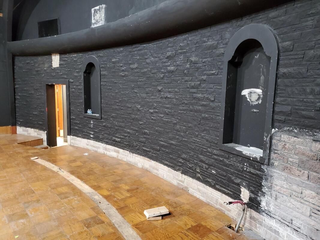 Dimly lit curved brick corridor with arched doorways and a wet floor