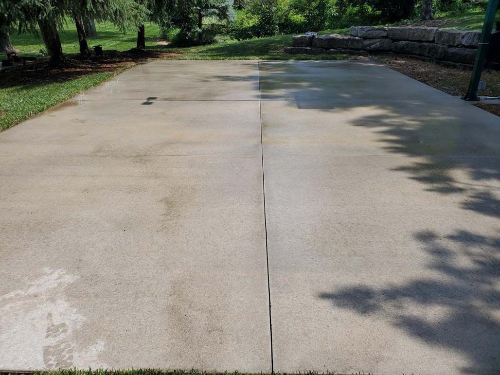 Concrete path in a park with trees and stone walls on both sides, partly shaded by sunlight.