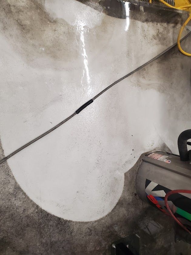 Concrete wall with a crack or cable line, plus a gray tool or device on the floor with wires nearby.