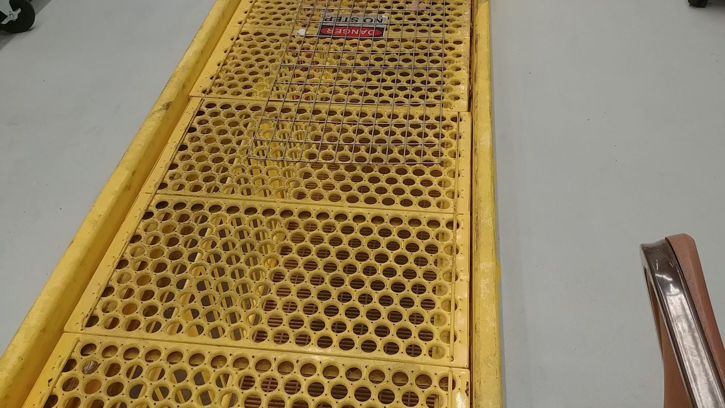 Yellow perforated metal platform ramp with a raised edge, viewed from above indoors
