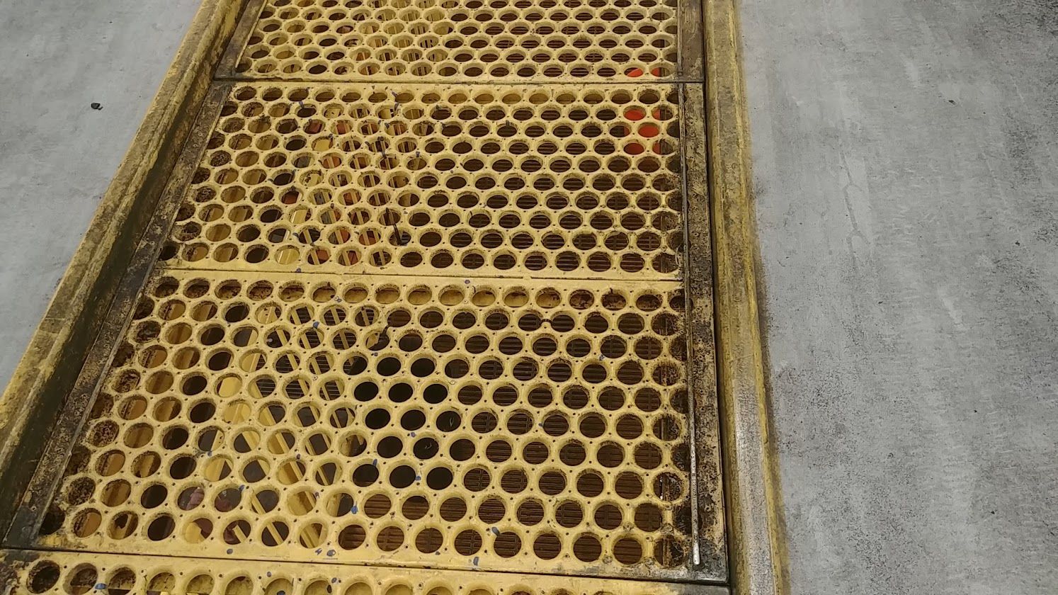 Yellow metal grated walkway with circular holes beside a gray concrete surface.