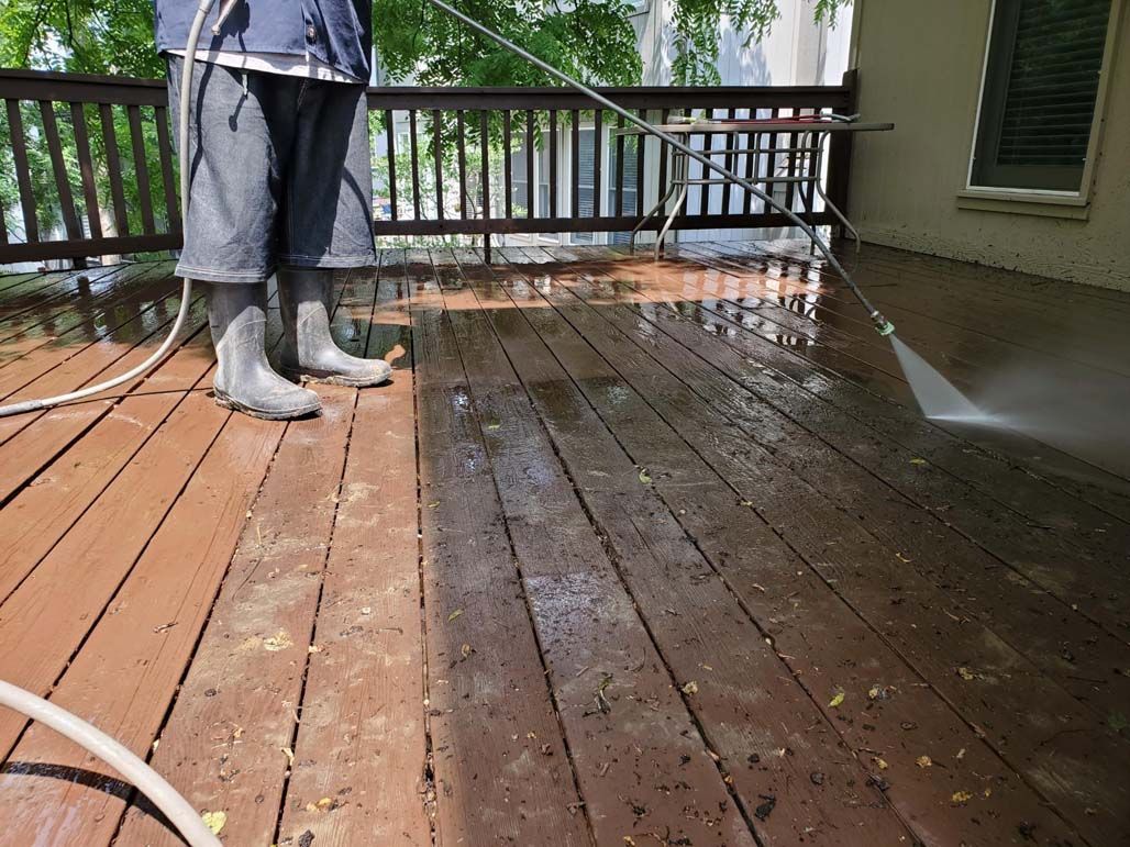 Person pressure-washing a wet wooden deck with a hose.