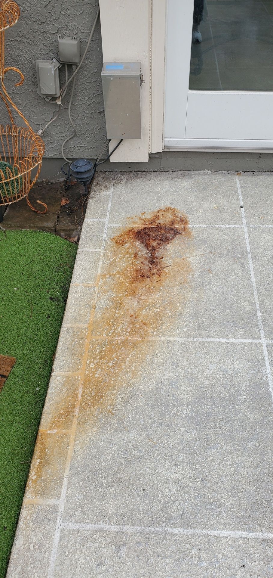 Rust-colored stain on a light gray concrete walkway beside a house door and artificial grass.