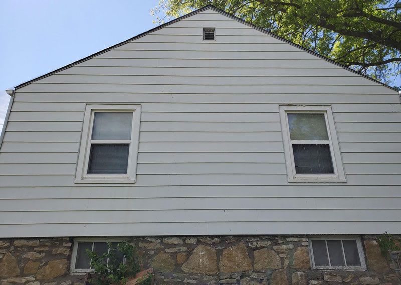 White house side wall with two windows and stone foundation under a blue sky