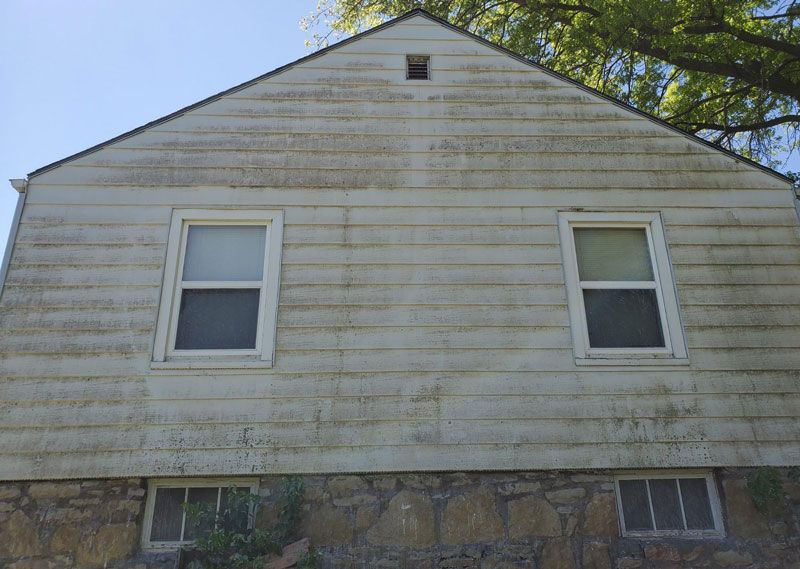 Weathered white house exterior with two upper windows and basement windows under a peaked roof
