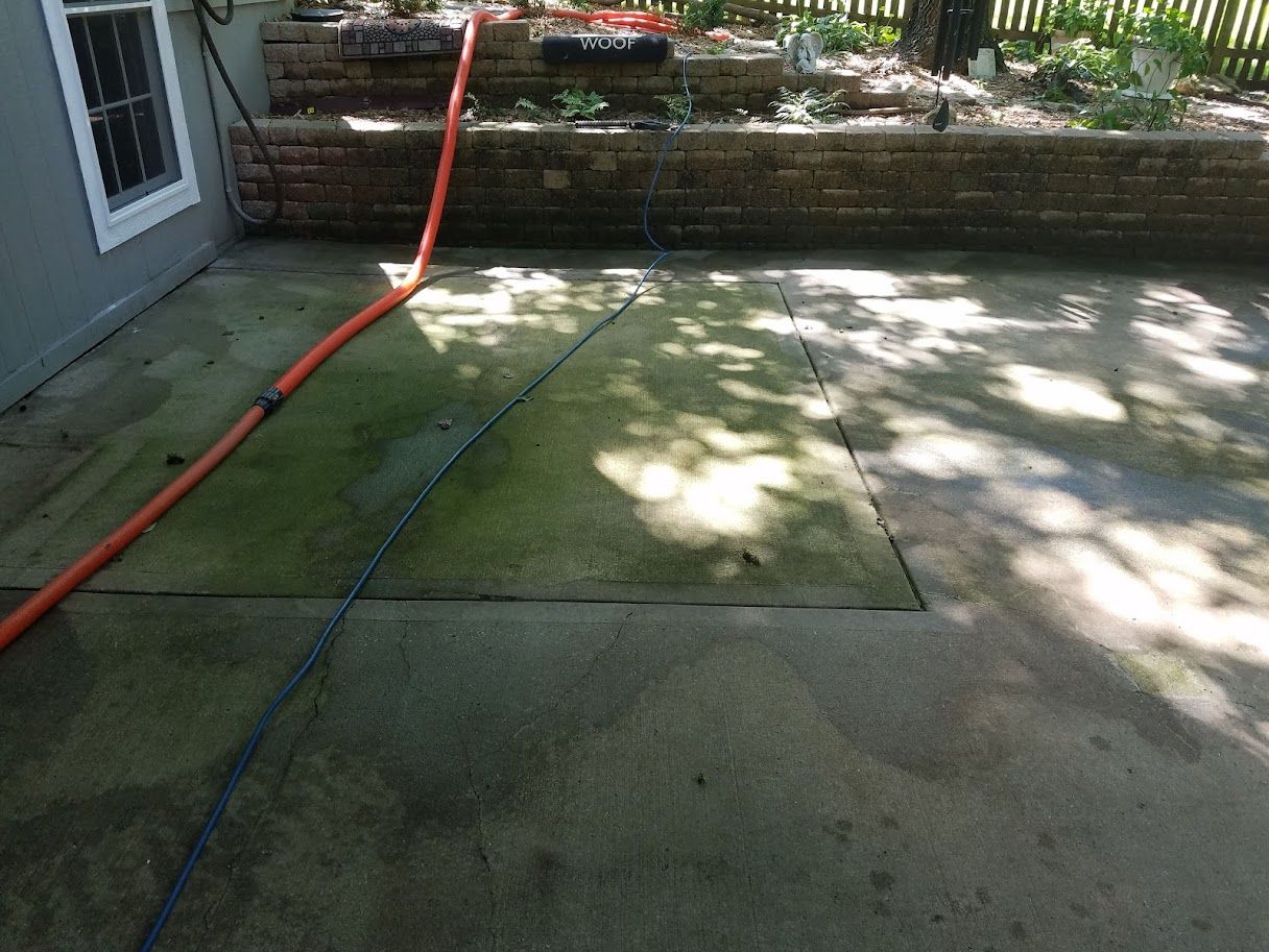 Backyard patio with a red hose on concrete and stone wall in dappled sunlight