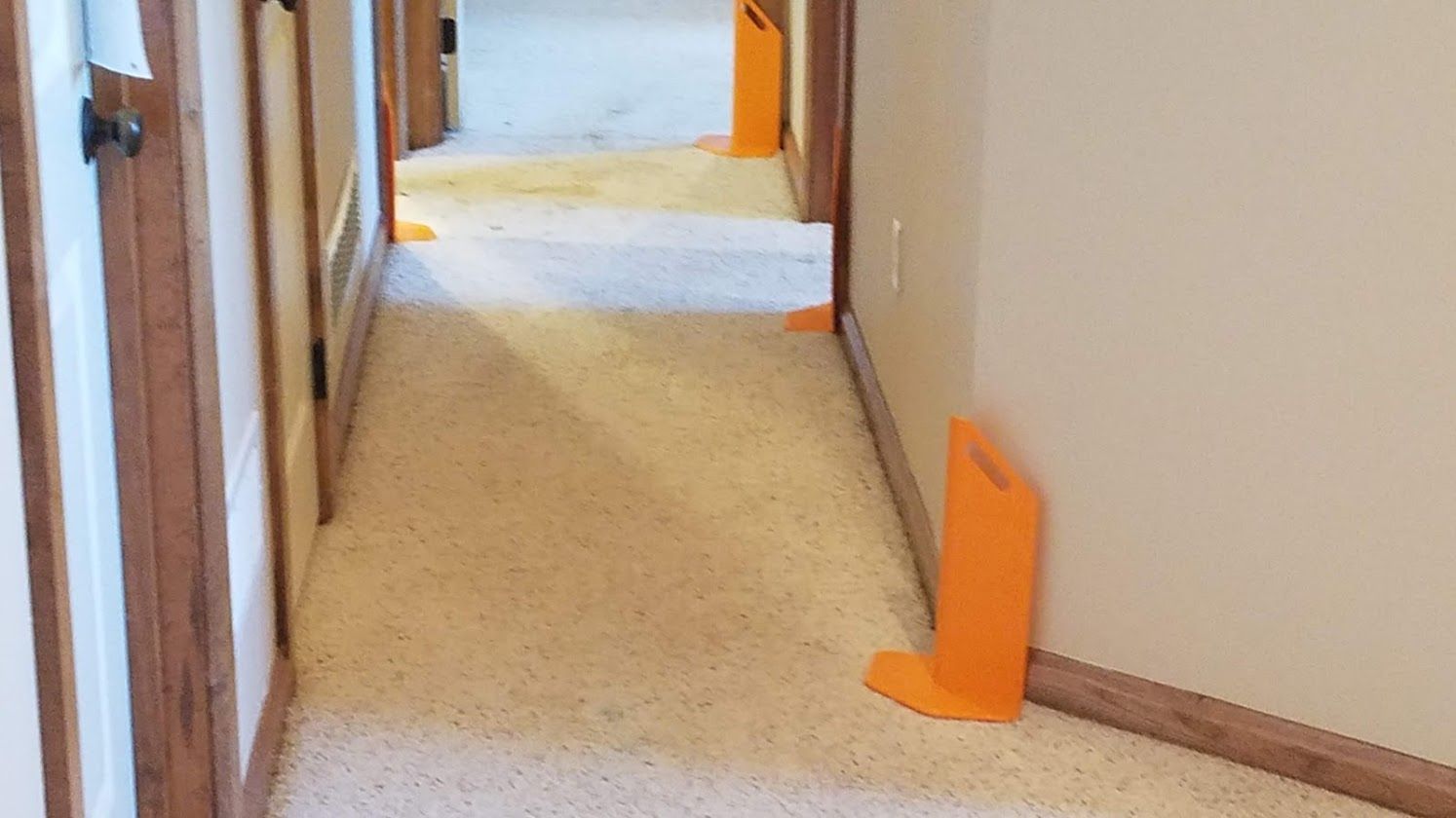 Narrow hallway with orange floor markers and beige walls, viewed toward an open doorway.